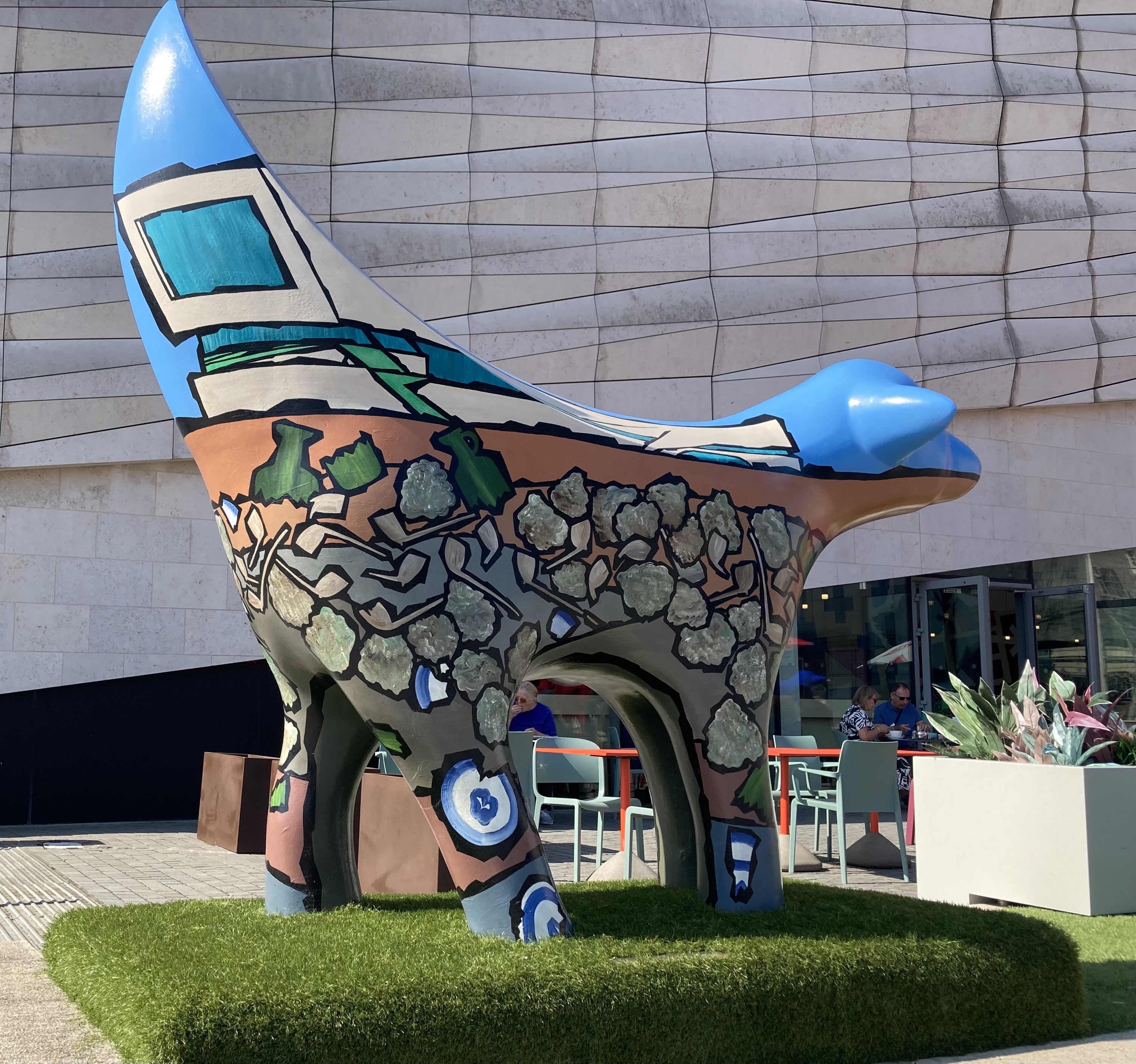 Statue with a lamb front and a banana shaped tail, with cartoon designs of archaeology painted on.